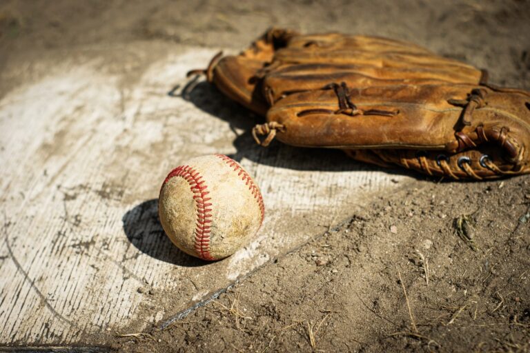 A vintage baseball glove and dirty ball laying on home plate. The plate is covered in dirt from a game.